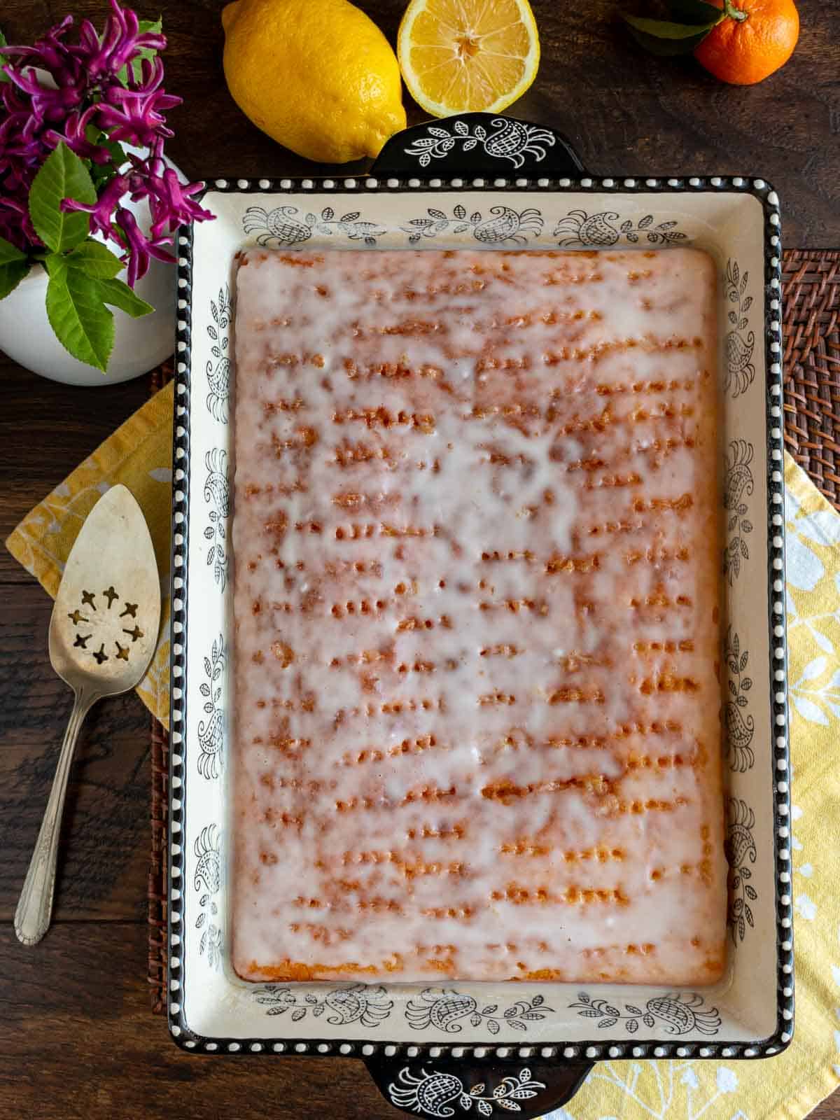 Baked lemon jello poke cake in a sheet pan surrounded by fresh lemons.