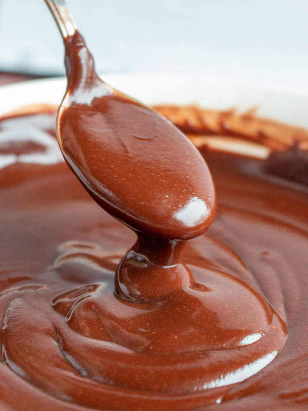 Spoon of thick chocolate pudding getting drizzled into a white bowl.