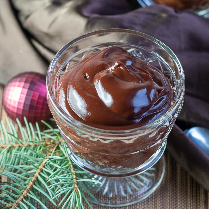 One close up shot of chocolate pudding in a clear cup with holiday ornaments and a brown silky cloth on the table. 
