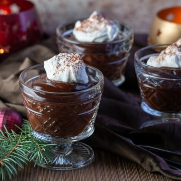 3 cups of chocolate pudding in glass dishes with a dollop of coconut whipped topping and a holiday scene.