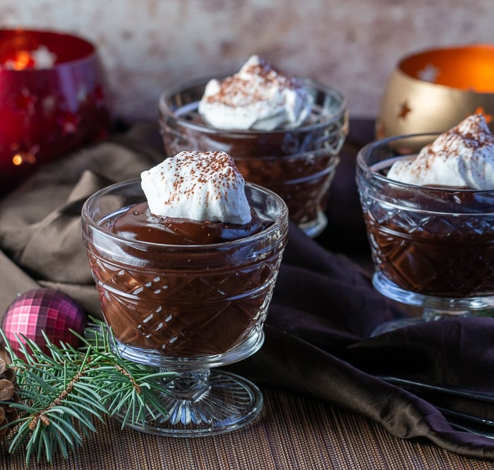3 cups of chocolate pudding in glass dishes with a dollop of coconut whipped topping and a holiday scene.