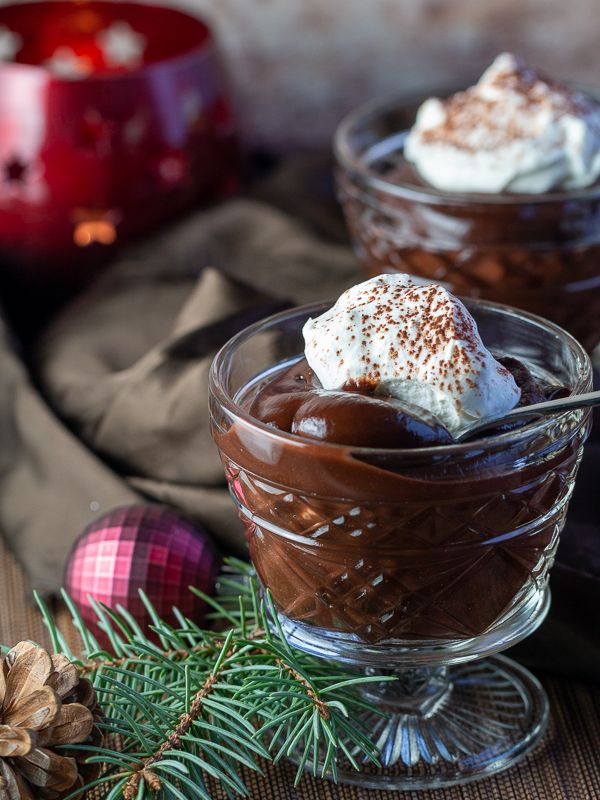 2 cups of chocolate pudding in glass dishes with a dollop of coconut whipped topping and a holiday scene.