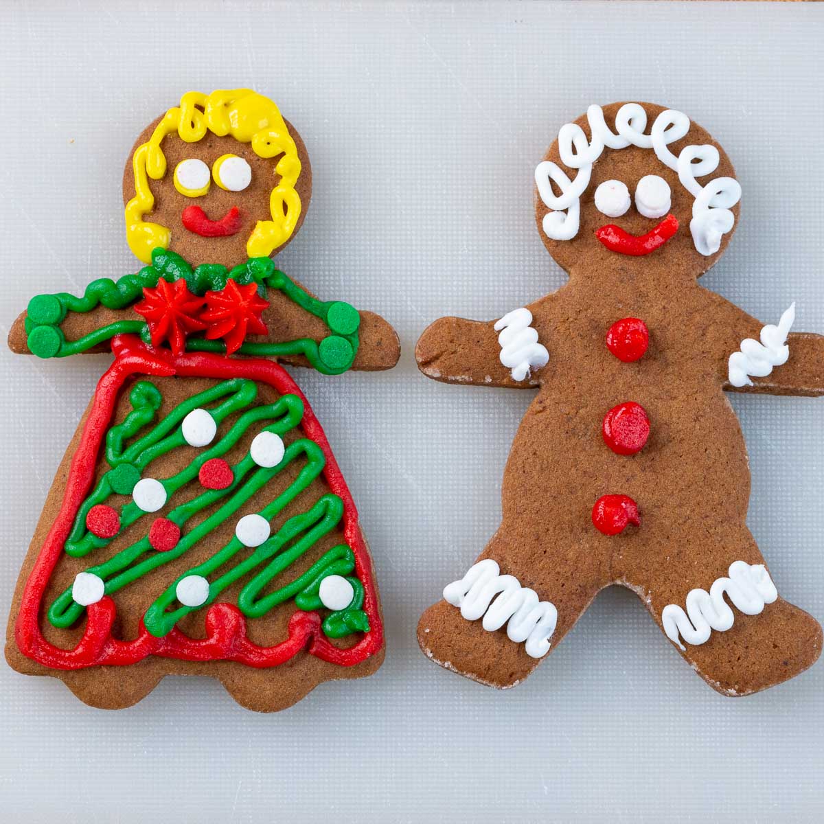 Decorated gingerbread man and gingerbread women on a white cutting board.