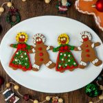 4 adorable gingerbread men and women on a white plate all holding hands.