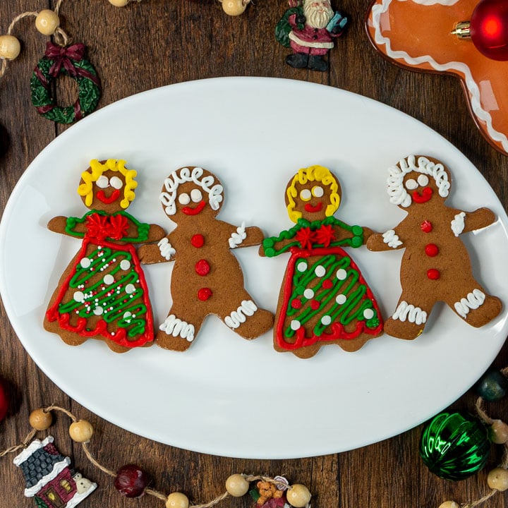 Homemade gingerbread cookies all decorated men and women holding hands on a white plate.