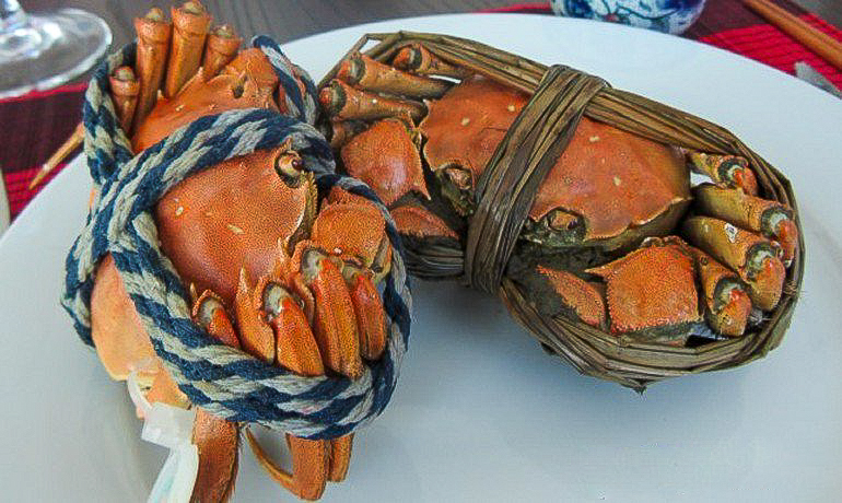 Male and female cooked hairy crabs on a white plate, tied up. 