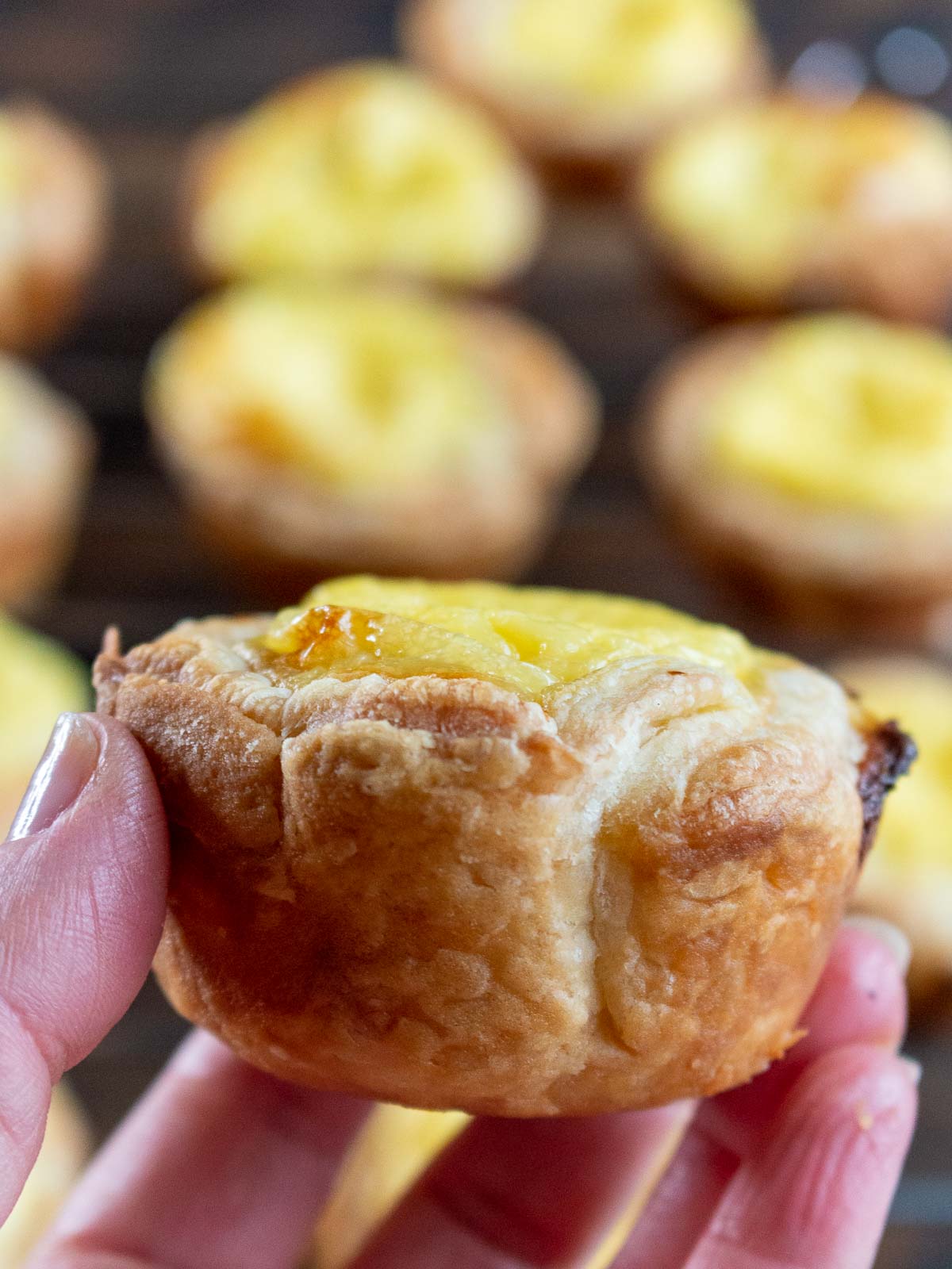 Holding a Hong Kong Style egg tart in the air showing the golden puff pastry dough.
