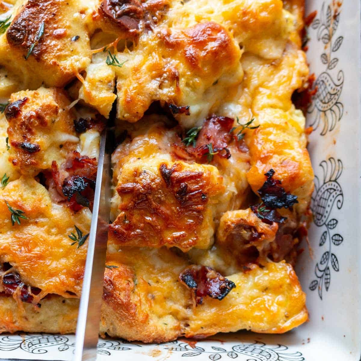 Cutting a slice of baked savory bread pudding from the 9 x 13 baking dish.