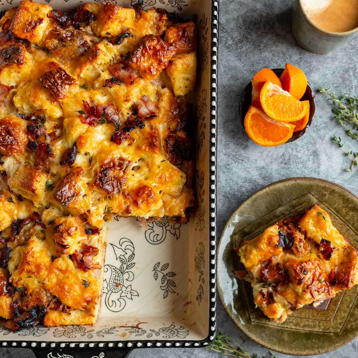 Baked savory breakfast bread pudding baked with a slice taken out and placed on a green plate with fresh oranges and coffee. 