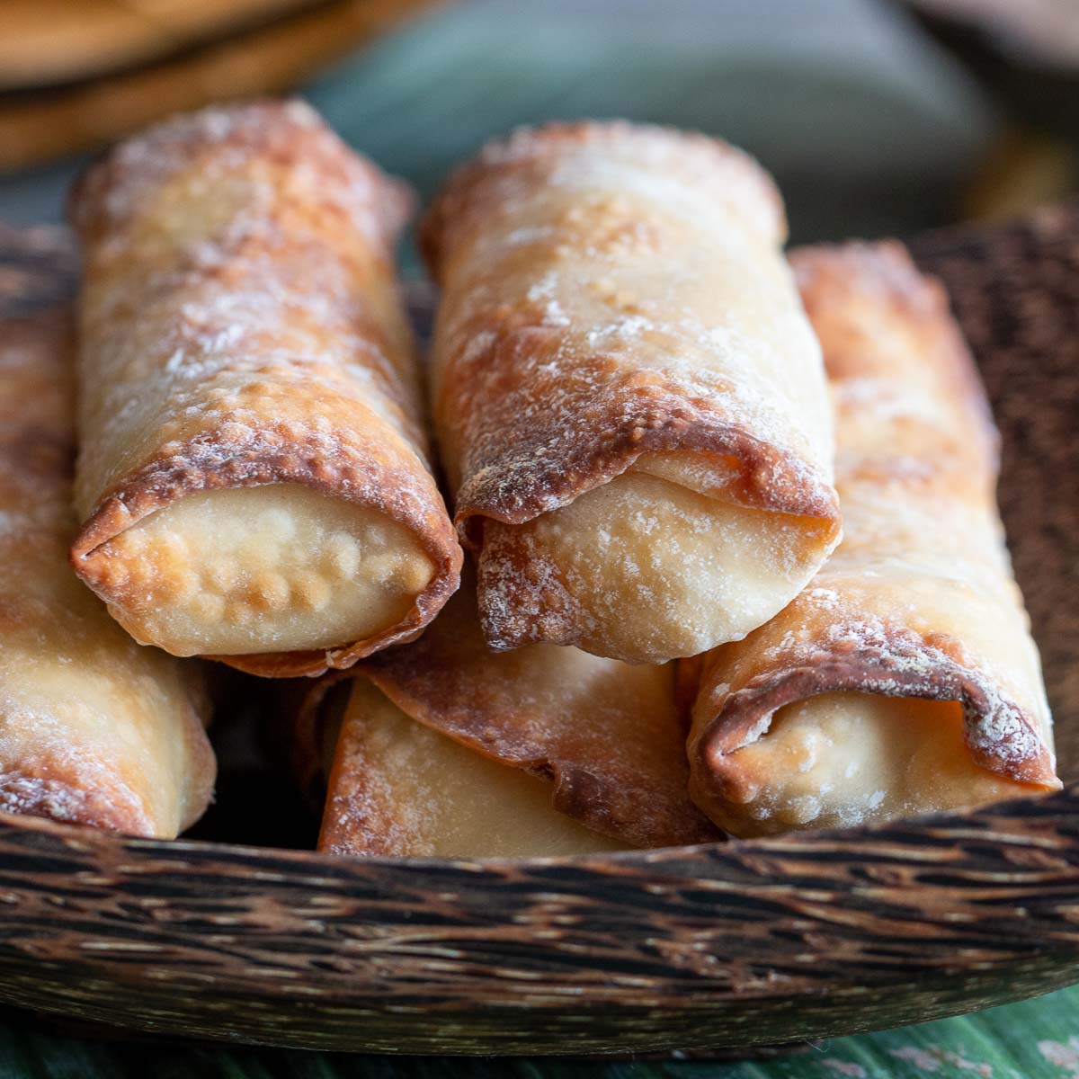 Stack of air fried spring rolls in wooden bowl.