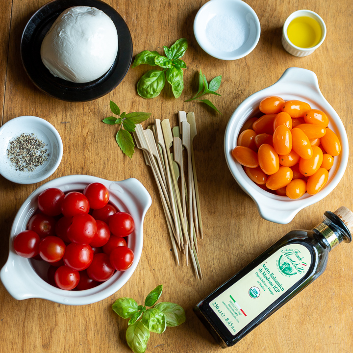 Ingredients of fresh mozzarella, cherry tomatoes, balsamic, EVOO and skewers on a wooden board.  