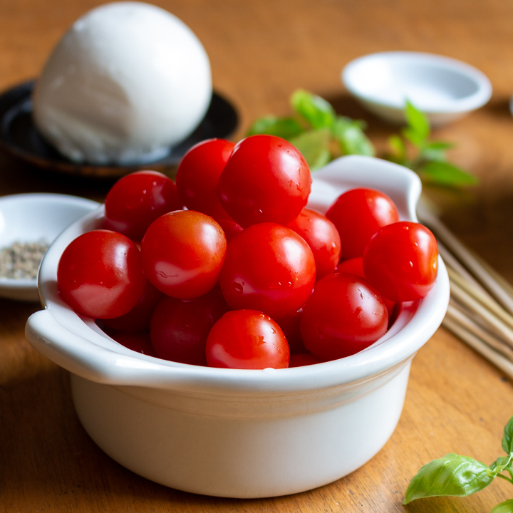 Red Cherry Tomatoes in a white bowl with basil garnish on the side.