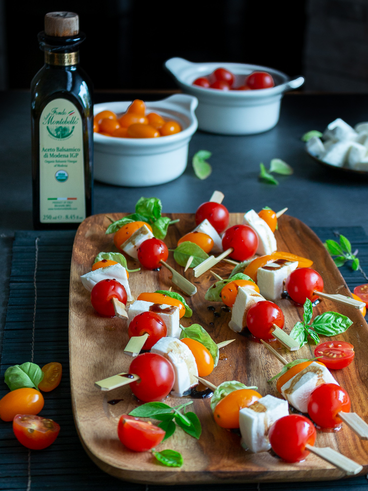 Caprese Skewers on a stick ready to eat with a bottle of balsamic vinegar in the background.