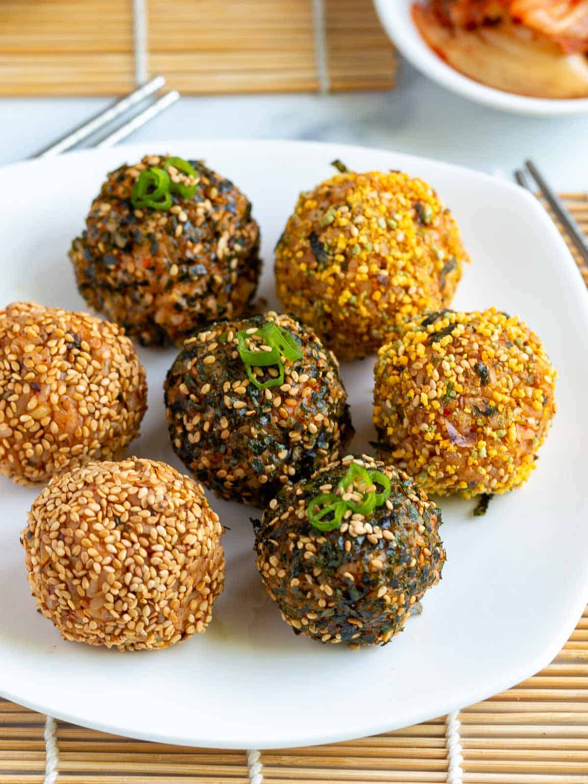 Showing 7 Korean Rice Balls on a  white plate with a side of kimchi. 