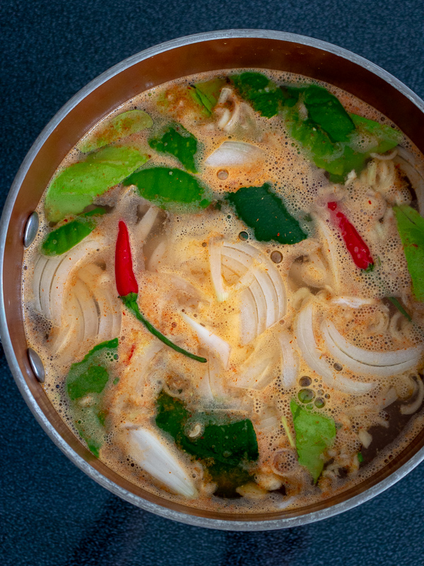 Kaffir lime leaves, chilis, and other aromatics in a soup pot. 