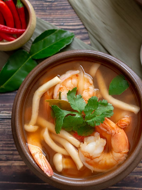 Tom Yum Goong garnished with coriander in a brown bowl. 