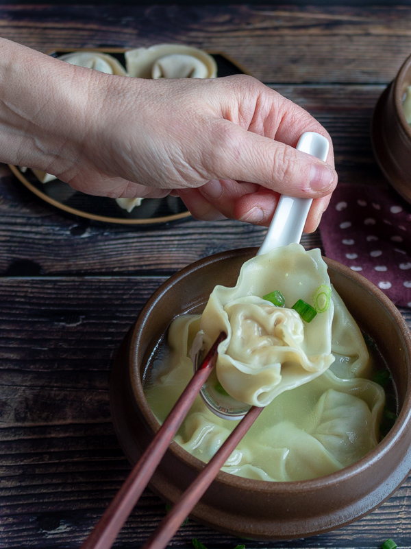Cooked Shanghai wonton in a Chinese spoon getting picked up with chopsticks with a tasty broth. 