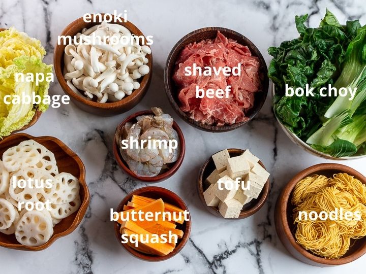 Mushrooms, beef, green leafy vegetables, tofu, and lotus root in wooden bowls.