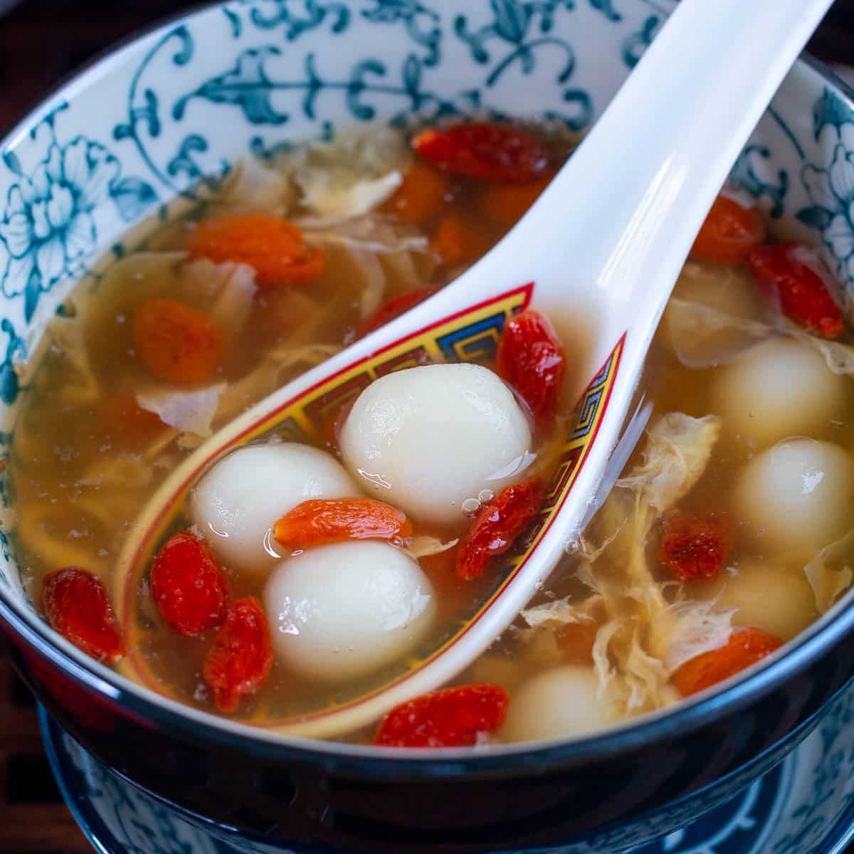 Scoop of the osmanthus sweet soup in a Chinese spoon with 3 tang yuan and goji berries.