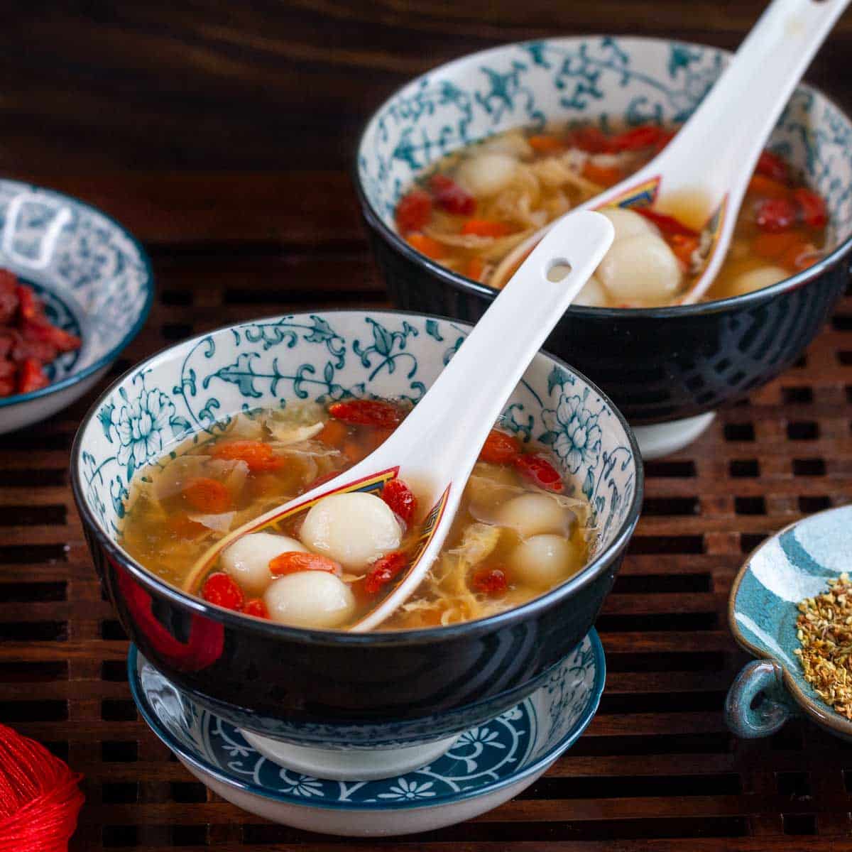 2 bowls of tang yuan soup hot and ready to eat with a bowl of osmanthus flowers and extra goji berries on the side.