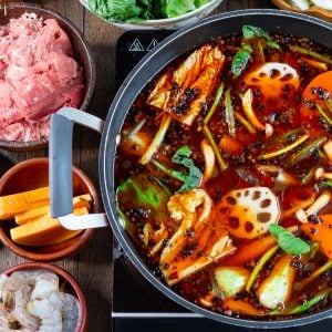 Spicy Sichuan Hot Pot cooking with vegetables and beef and other vegetables around the hot pot in bowls.