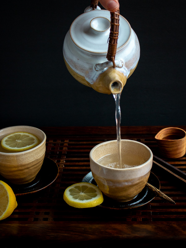 Pouring tea from a beige and white hand made pottery tea kettle into matching handmade beige pottery cups. 