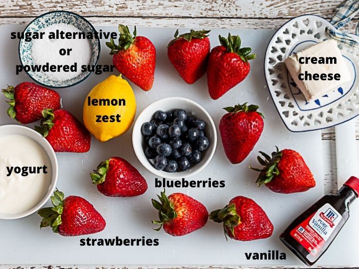 Ingredients; cream cheese, strawberries, blueberries, lemon zest, sugar, vanilla and yogurt laid out on cutting board.