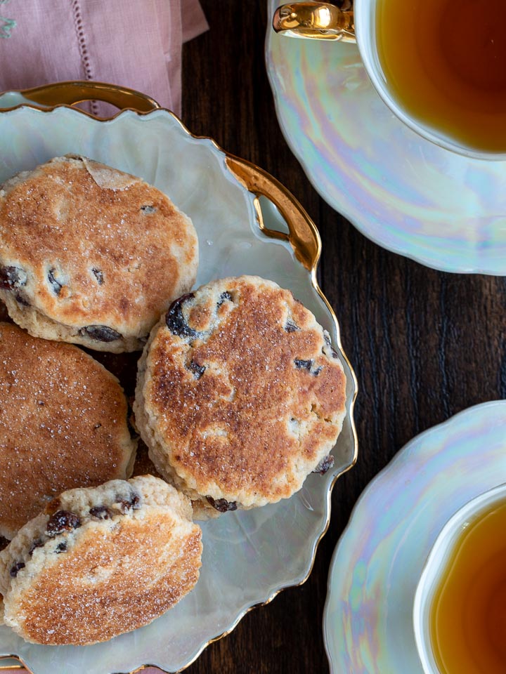 Overhead shot showing two cups of tea served with hot Welsh Cakes.