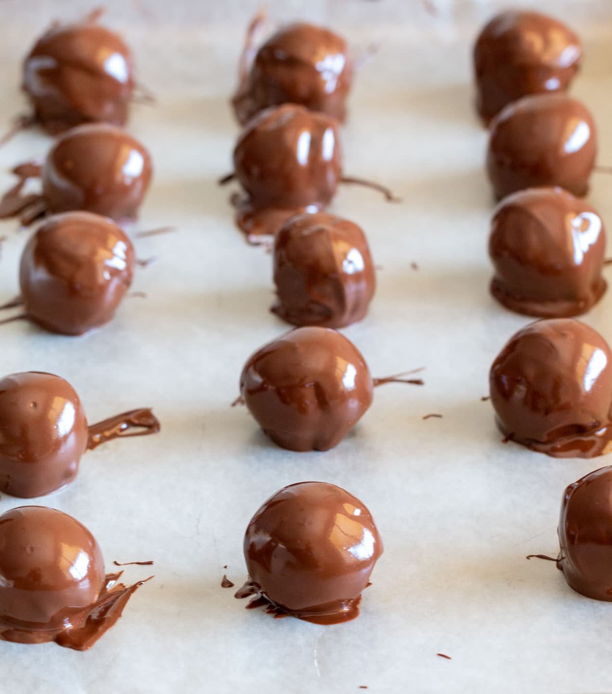 No bake mint Oreo balls freshly dipped in chocolate on a parchment lined baking tray.