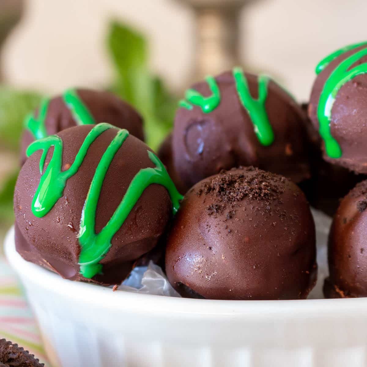 Some dairy free oreo truffles decorated with Oreo crumbles and some with green icing in a white bowl. 