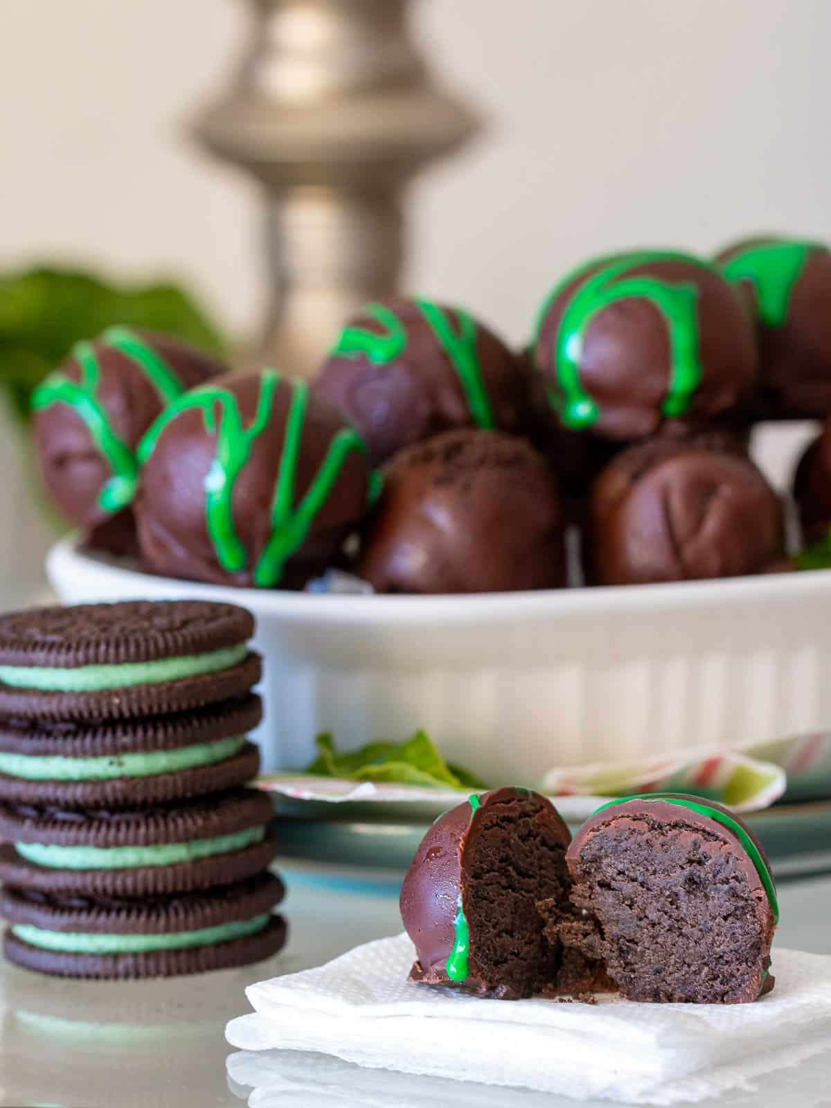 One mint Oreo truffle cut in half with a bowl of them whole and a stack of Oreo cookies. 