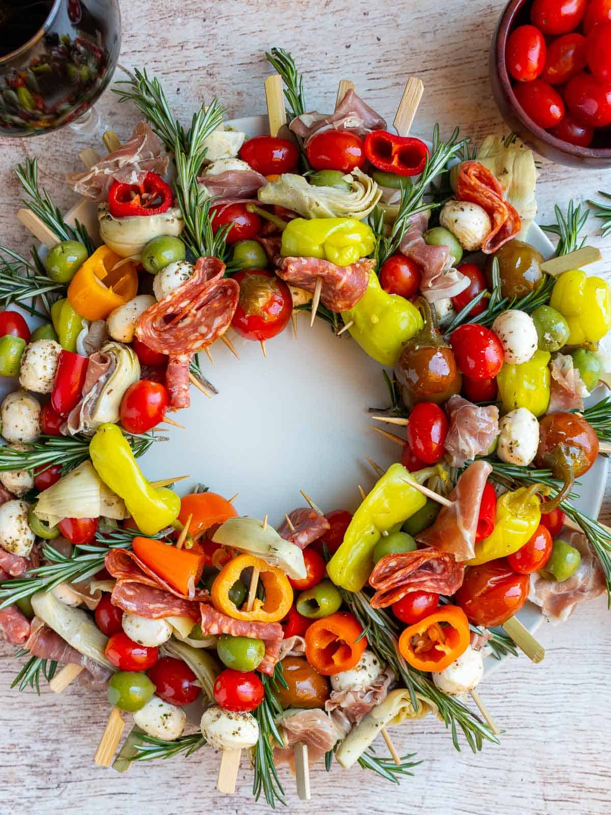 Italian Antipasto Wreath Charcuterie Skewers with 2 glasses of wine and tomatoes on the side,