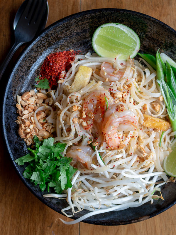 Pad Thai in a black bowl with all the garnishes.