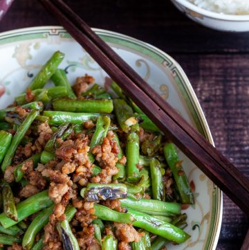 Stir fried dry fried green beans and minced pork in a Chinese bowl with wooden chop sticks and a side of rice.