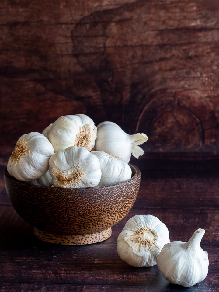 8 heads of garlic in a wooden bowl and 2 heads next to the bowl. 
