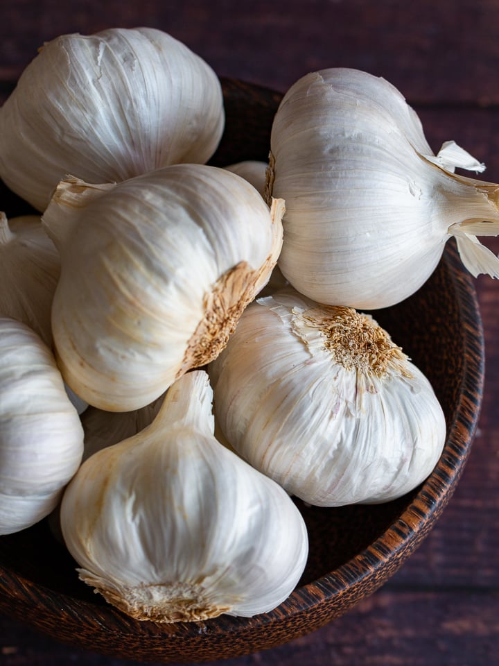 8 bulbs of garlic in a wooden bowl looking down into them with the soft light highlighting their white skin.