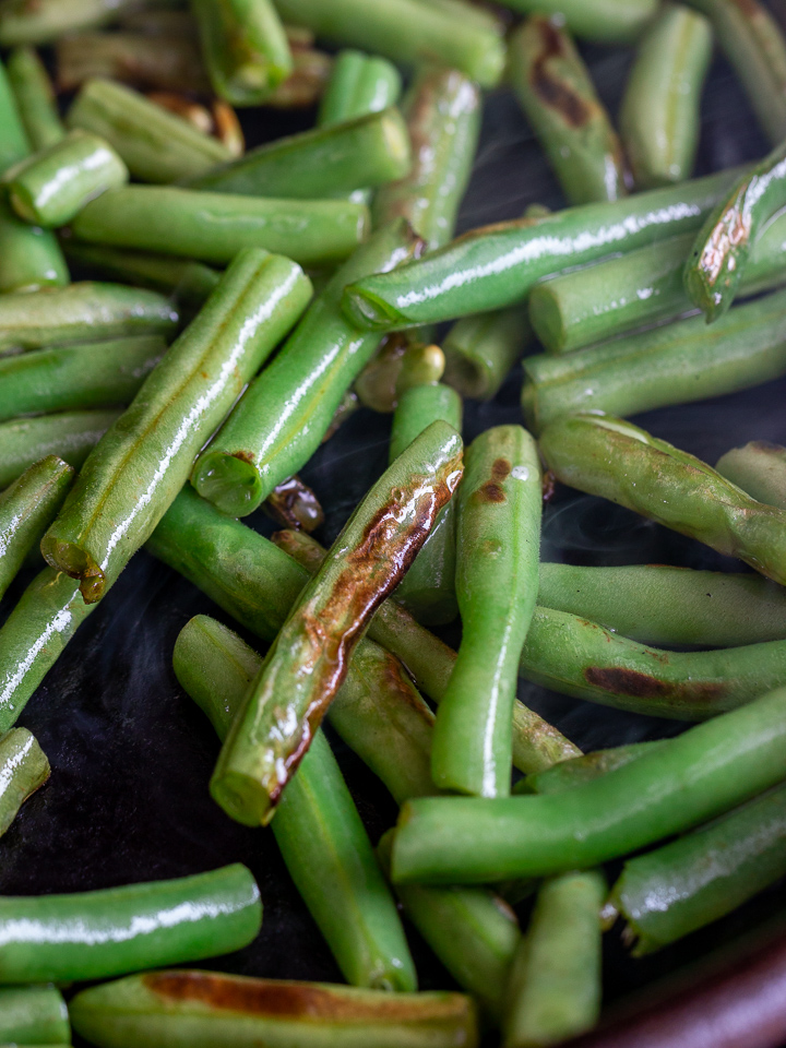 Green beans getting dry fried and seared in an iron skillet.