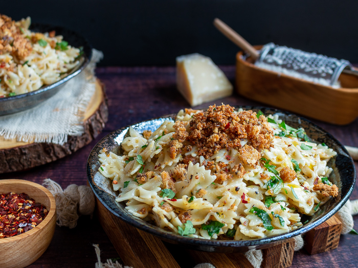 2 plates of Farfalle Aglio e Olio with Breadcrumbs with parmesan and red pepper flakes for extra garnishes.