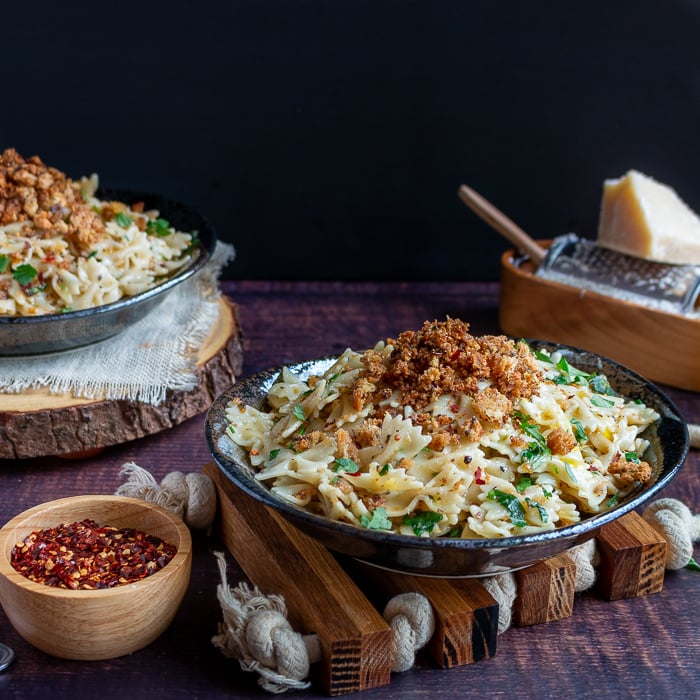 2 plates of Farfalle Aglio e Olio with Breadcrumbs with parmesan and red pepper flakes for extra garnishes. 