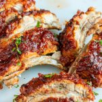 Cooked and sliced BBQ baby back ribs on a white cutting board.