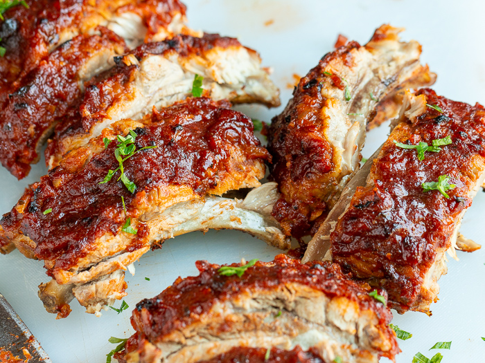 Cooked and sliced BBQ baby back ribs on a white cutting board.