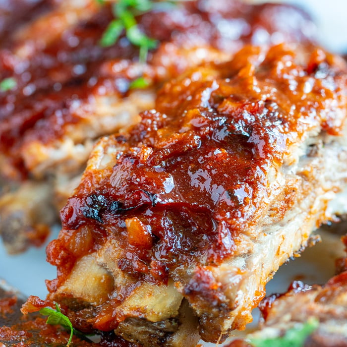 Two fall off the bone baby back ribs slathered with BBQ sauce.