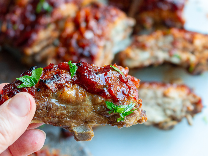 Holding one juicy BBQ rib in left hand and ready to take a bite into it.