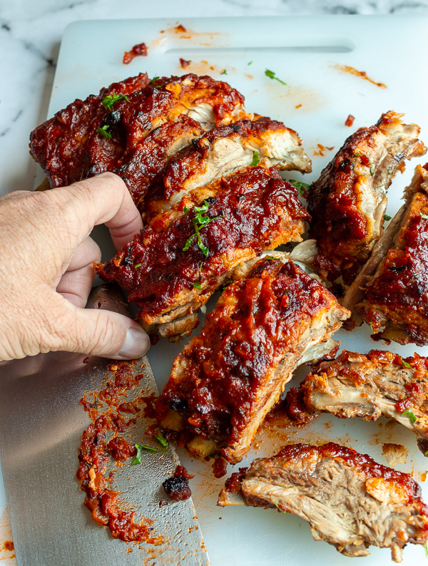 Someone grabbing one of the perfectly finger licking good ribs off the cutting board. 