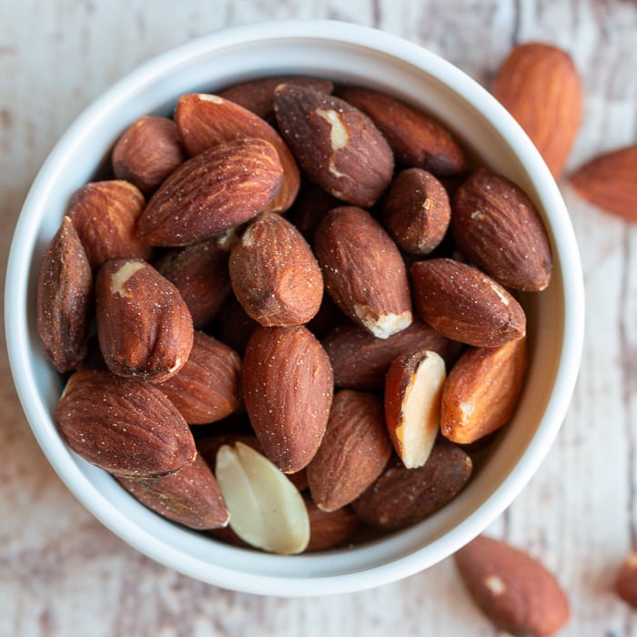 Toasted whole almonds in a white bowl. 