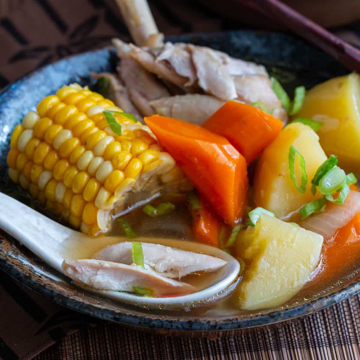 Showing a Chinese spoonful of clear ABC soup broth with tender chicken with the vegetables in a black bowl.