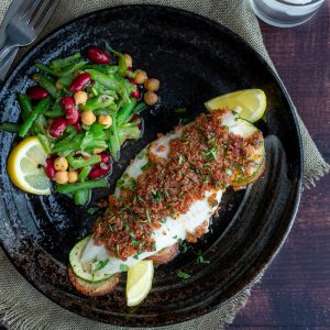 Top down photo of Baked Chorizo crusted fish served with lemons and a three bean salad.