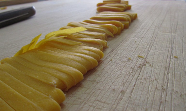 Tagliatelle freshly cut on a wooden cutting board.