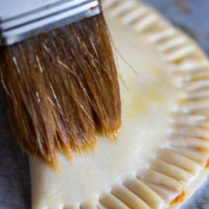 Brushing top of empanadas with egg wash.