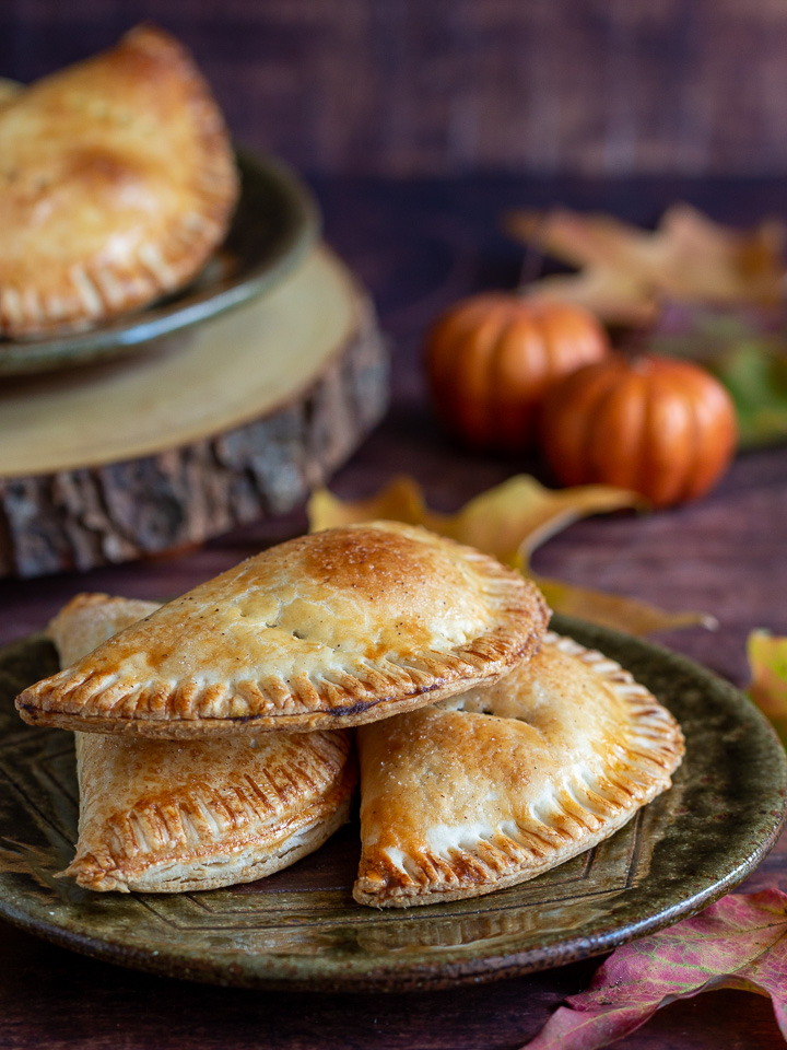 3 pumpkin empanadas on a green plate with little pumpkins in the background.